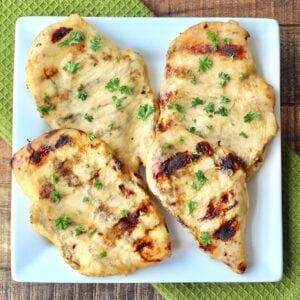 Four pieces of grilled honey mustard chicken on plate garnished with parsley.