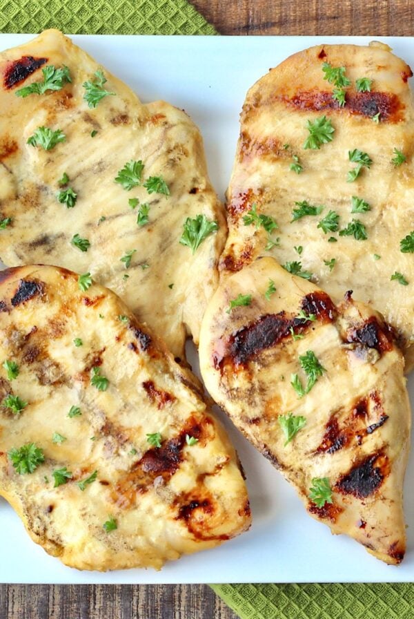 Four pieces of grilled honey mustard chicken on plate garnished with parsley.