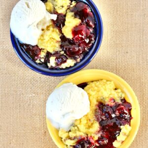 Two bowls filled with lemon blueberry dump cake and a scoop of vanilla ice cream on the side.