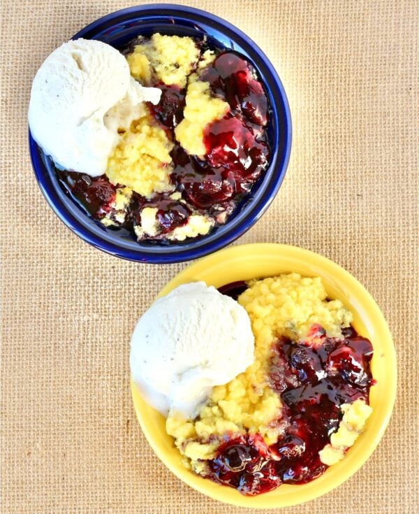 Two bowls filled with lemon blueberry dump cake and a scoop of vanilla ice cream on the side.