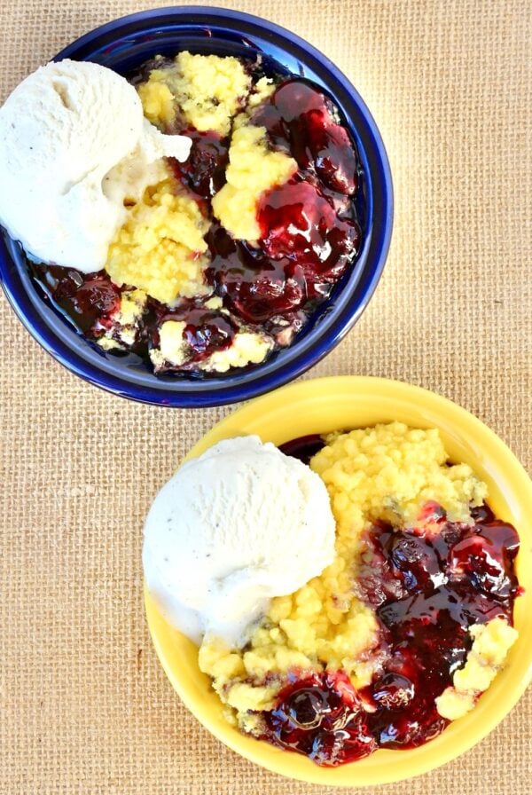 Two bowls filled with lemon blueberry dump cake and a scoop of vanilla ice cream on the side.