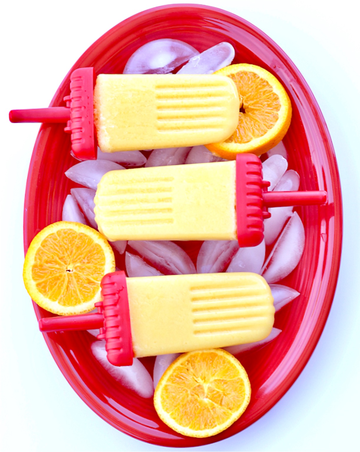 Three orange creamsicle popsicles on plate with ice and orange slices.