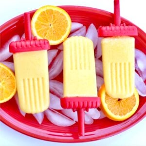 Homemade Orange Popsicles on plate with oranges and ice.