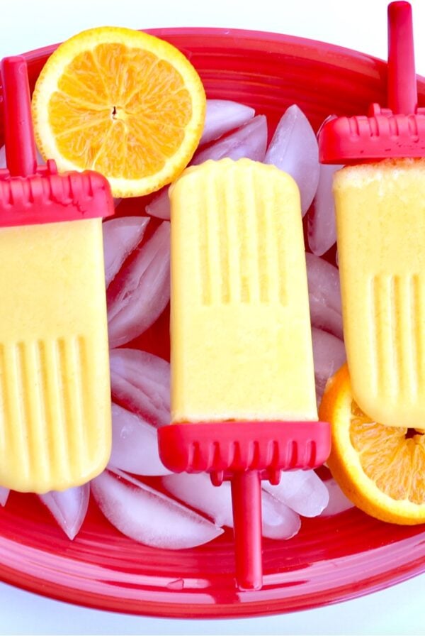Homemade Orange Popsicles on plate with oranges and ice.