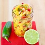 Pineapple mango salsa in mason jar, and lime and jalapeño pepper to the side.