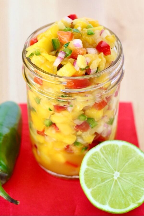 Pineapple mango salsa in mason jar, and lime and jalapeño pepper to the side.
