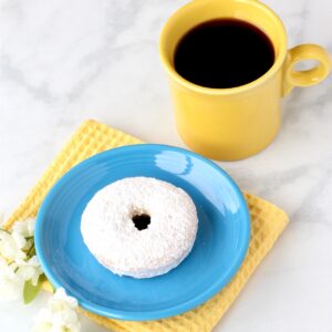 Powdered sugar donut on plate with cup of coffee to the side.
