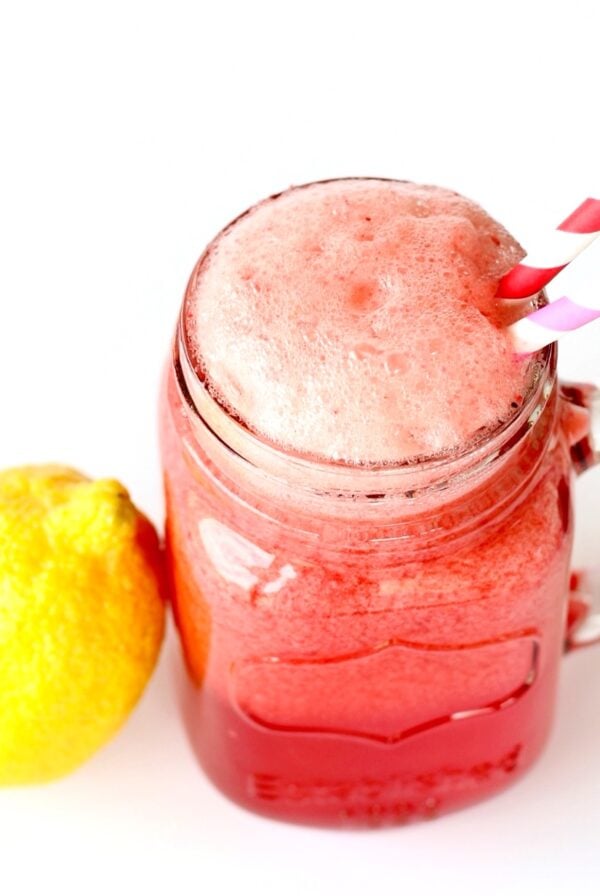 Sparkling raspberry lemonade in mason jar mug with straws, and lemon to the side.
