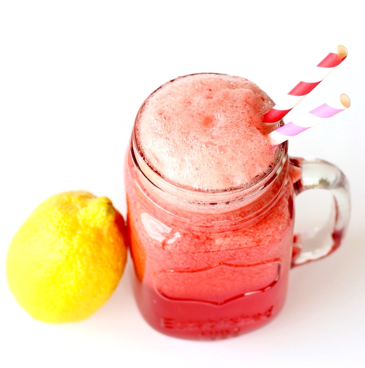 Sparkling raspberry lemonade in mason jar mug with straws, and lemon to the side.