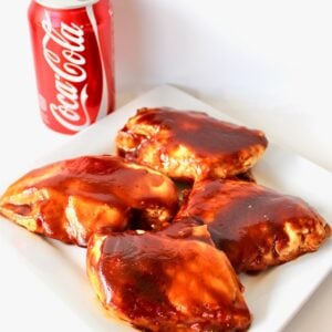 Four pieces of bbq Coca Cola chicken on plate with can of Coca-Cola in background.