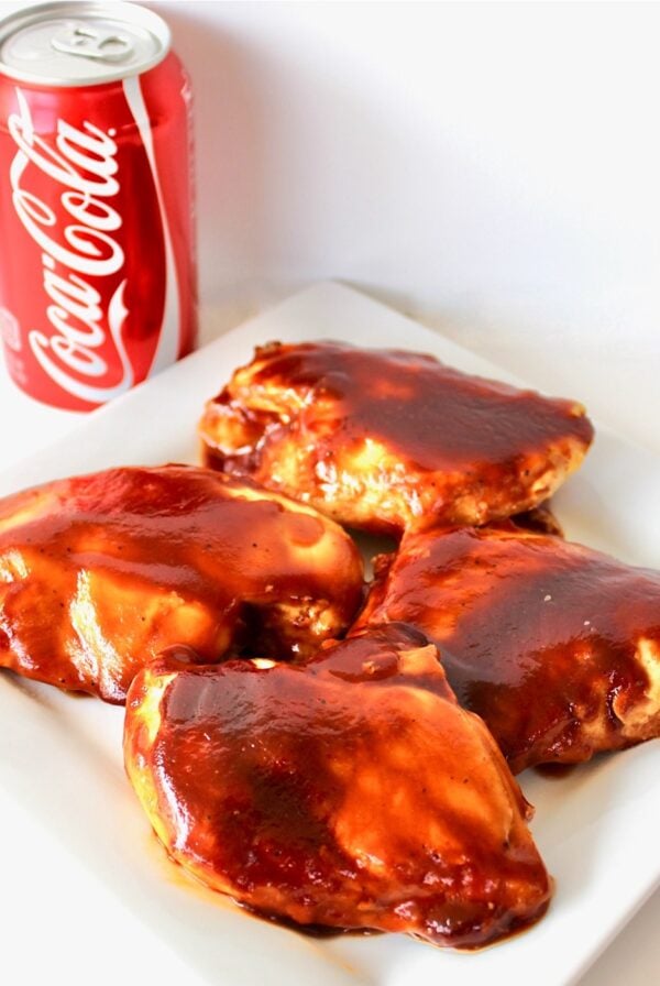 Four pieces of bbq Coca Cola chicken on plate with can of Coca-Cola in background.