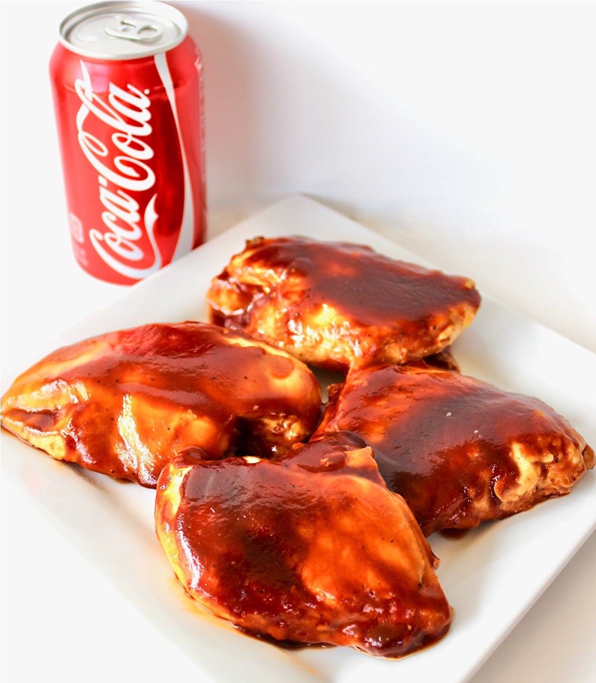 Four pieces of bbq Coca Cola chicken on plate with can of Coca-Cola in background.
