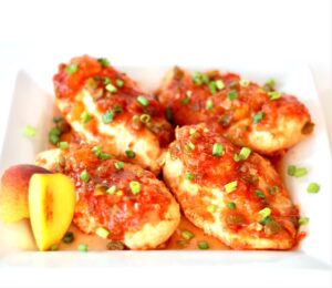 Four pieces of peach salsa chicken on plate with green onions, and fresh peach slices to the side.