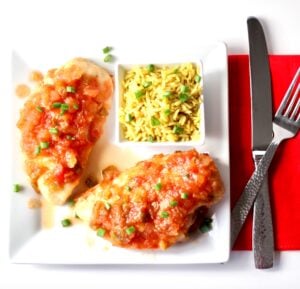 Two pieces of pineapple salsa chicken on plate with rice on the side.