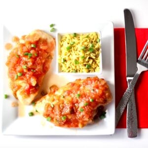 Two pieces of pineapple salsa chicken on plate with rice on the side.