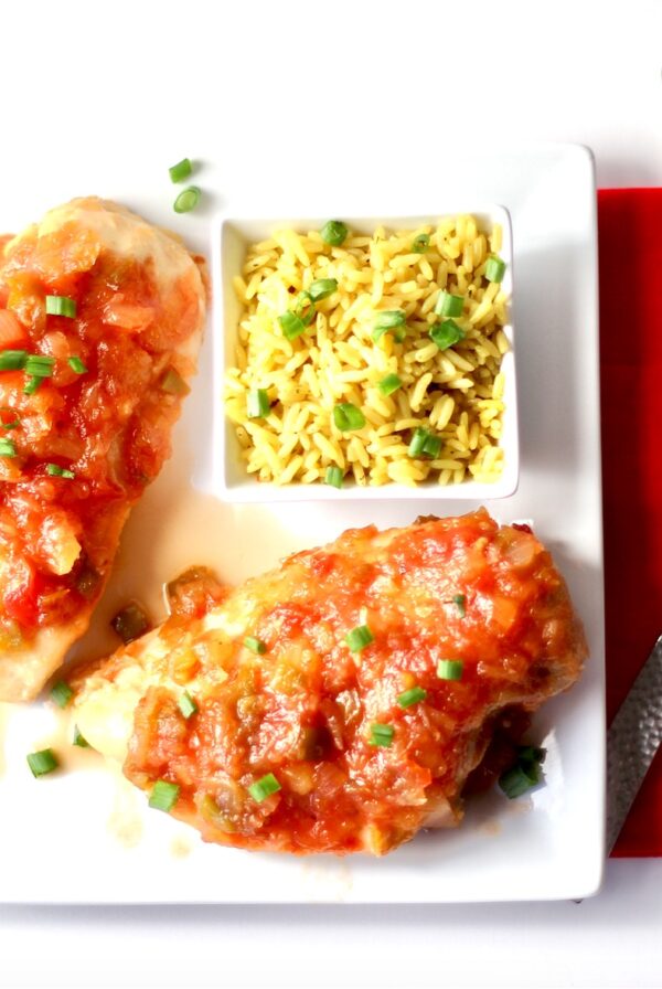 Two pieces of pineapple salsa chicken on plate with rice on the side.