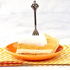 Slice of pumpkin pie cheesecake with whip cream on top and fork inserted.