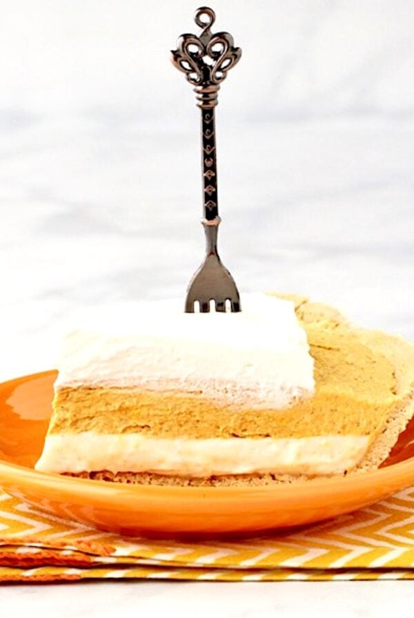 Slice of pumpkin pie cheesecake with whip cream on top and fork inserted.