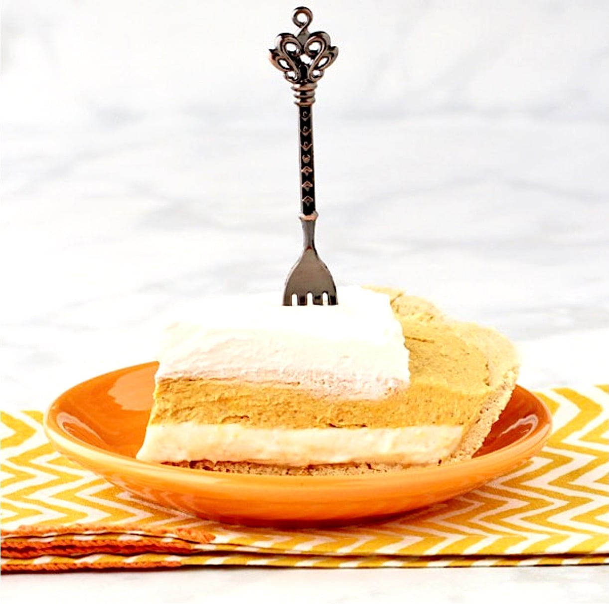 Slice of pumpkin pie cheesecake with whip cream on top and fork inserted.