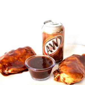 Two pieces of root beer chicken on plate with barbecue sauce and can of A&W root beer.