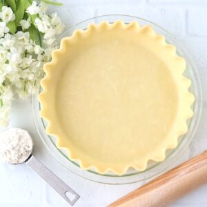 Homemade pie crust in pie dish with flour and rolling pin to the side.