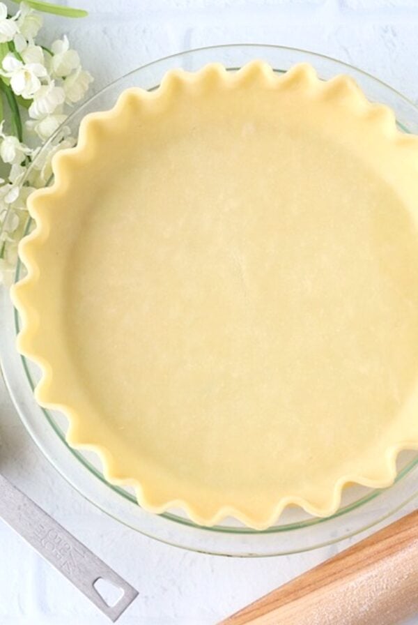 Homemade pie crust in pie dish with flour and rolling pin to the side.