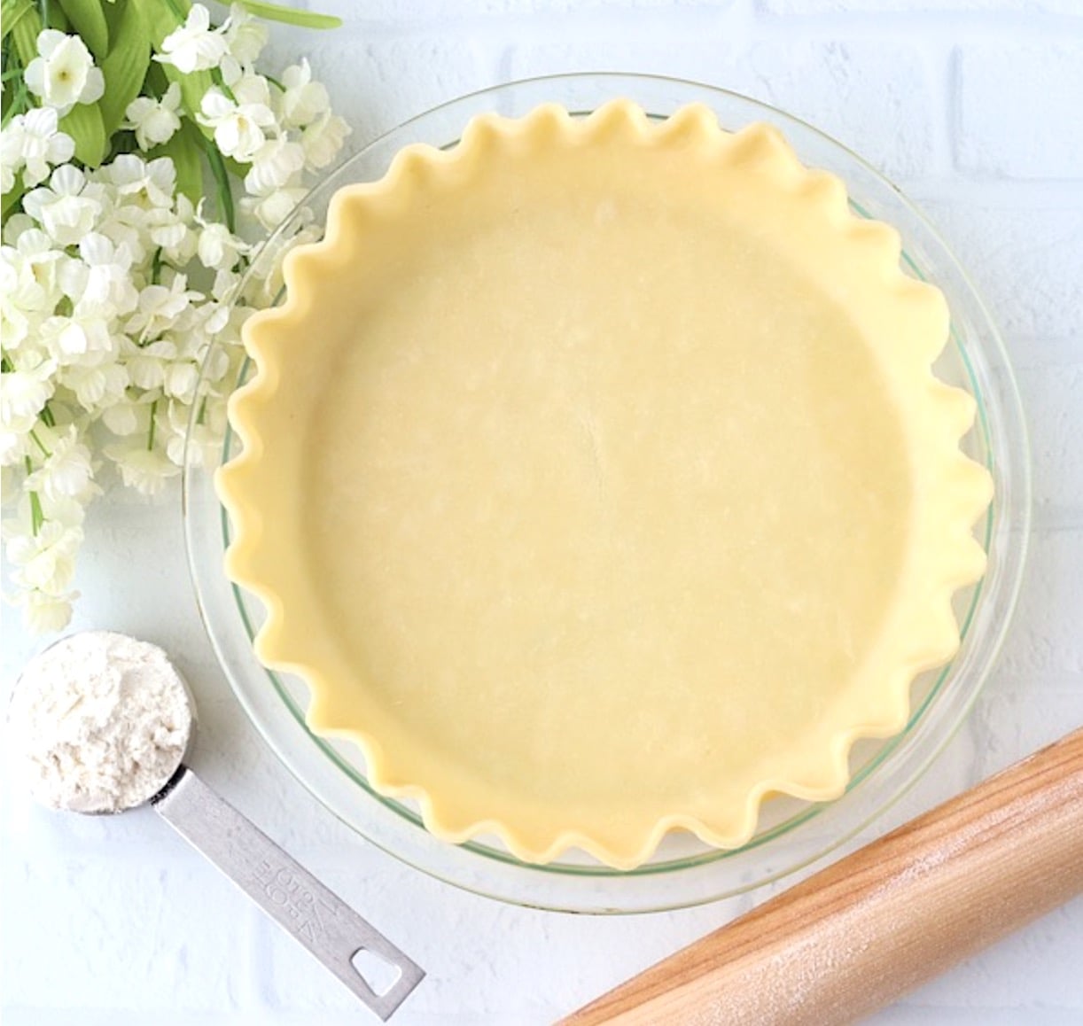 Homemade pie crust in pie dish with flour and rolling pin to the side.