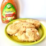 Three pieces of Italian Dressing chicken on plate with Italian Dressing bottle in background.