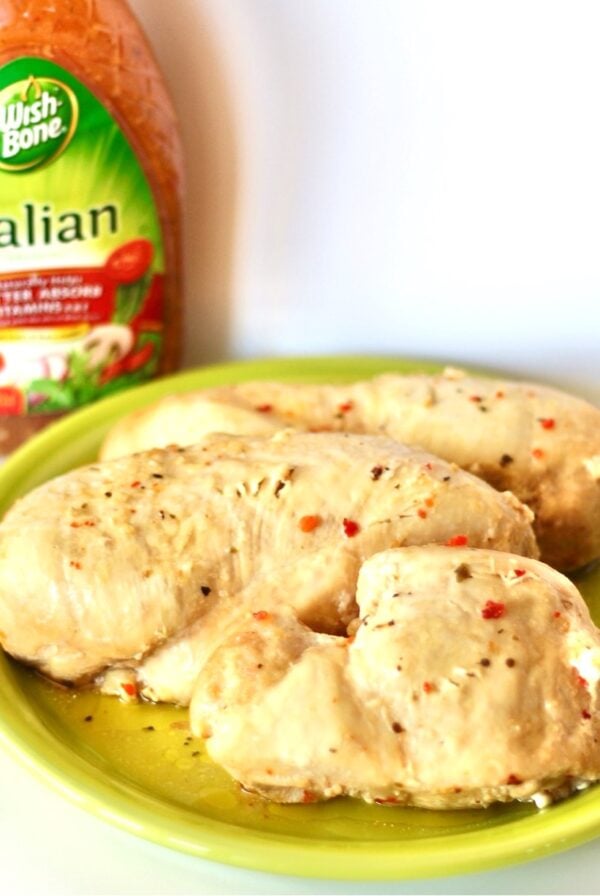 Three pieces of Italian Dressing chicken on plate with Italian Dressing bottle in background.