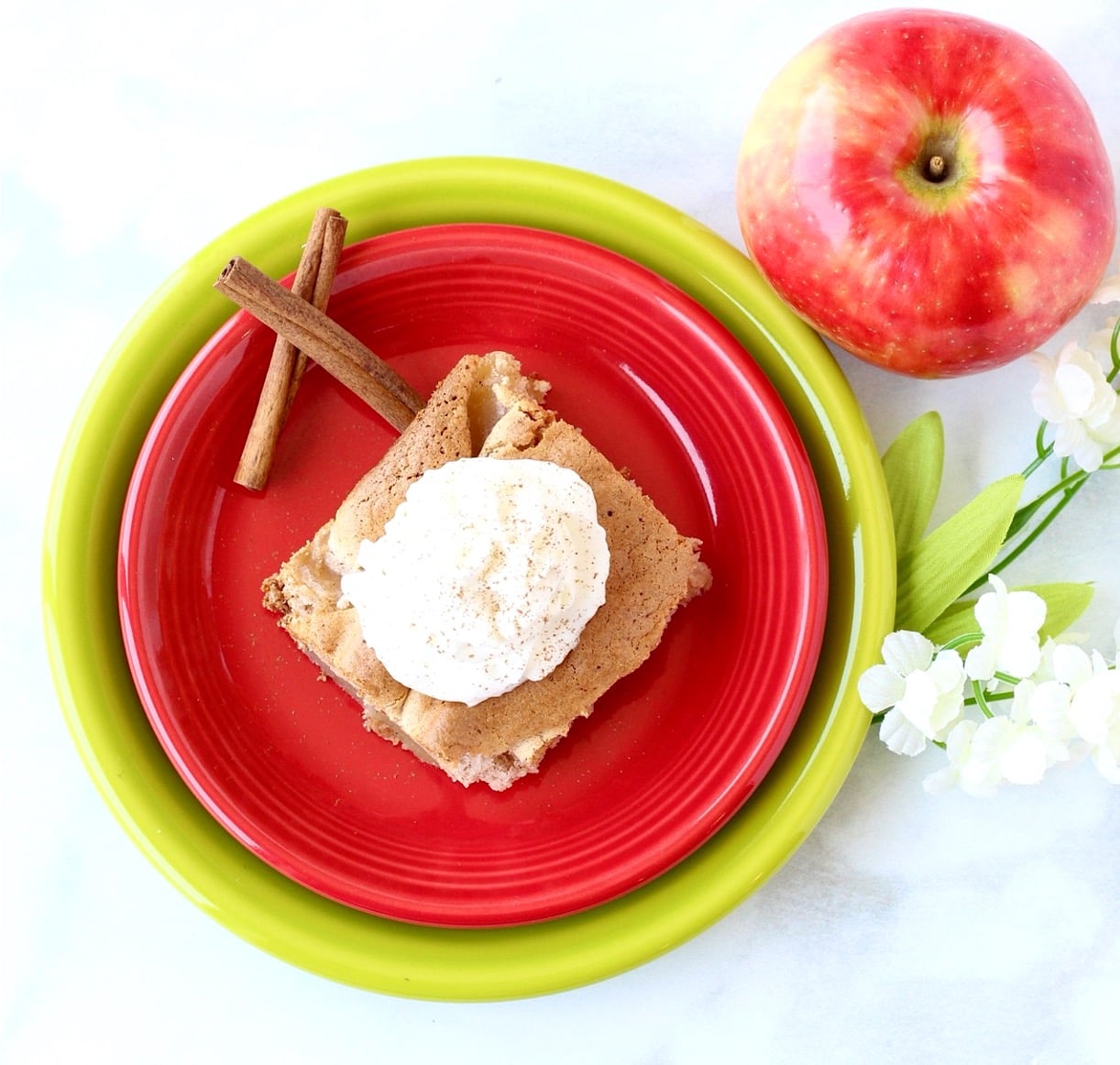 Apple cinnamon cake on plate with whip cream on top and cinnamon sticks to the side.