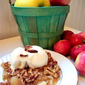 Apple cobbler made with cake mix on plate with ice cream, and apples in the background.