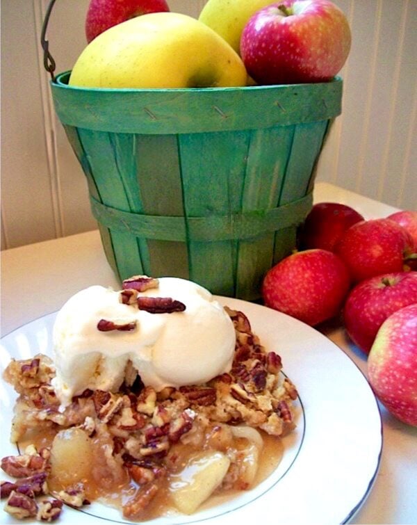 Apple cobbler made with cake mix on plate with ice cream, and apples in the background.