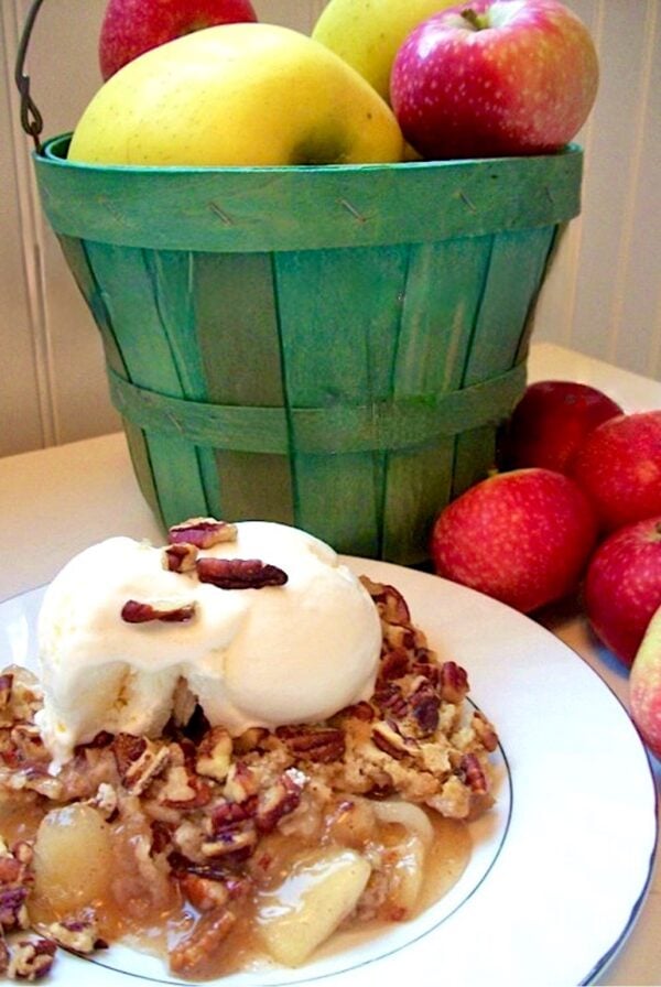 Apple cobbler made with cake mix on plate with ice cream, and apples in the background.