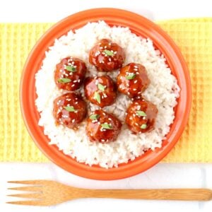 Asian meatballs garnished with sesame seeds and green onions on plate with rice.
