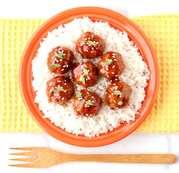 Asian meatballs garnished with sesame seeds and green onions on plate with rice.