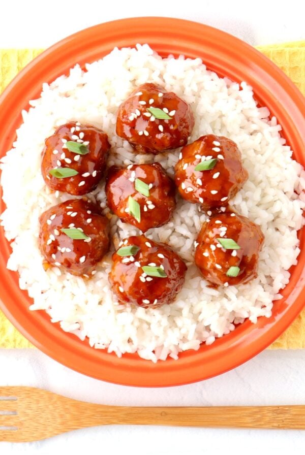 Asian meatballs garnished with sesame seeds and green onions on plate with rice.