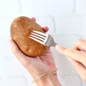 Fork poking holes in russet potato before baking in crock pot.