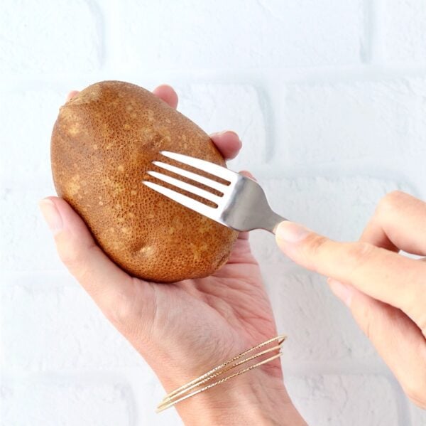 Fork poking holes in russet potato before baking in crock pot.