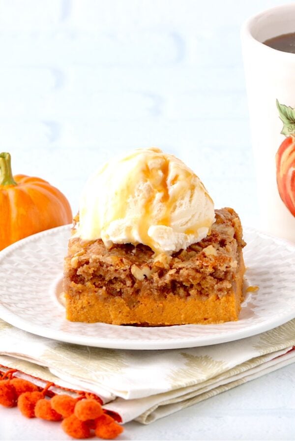 Piece of pumpkin dump cake on plate with scoop of ice cream on top.
