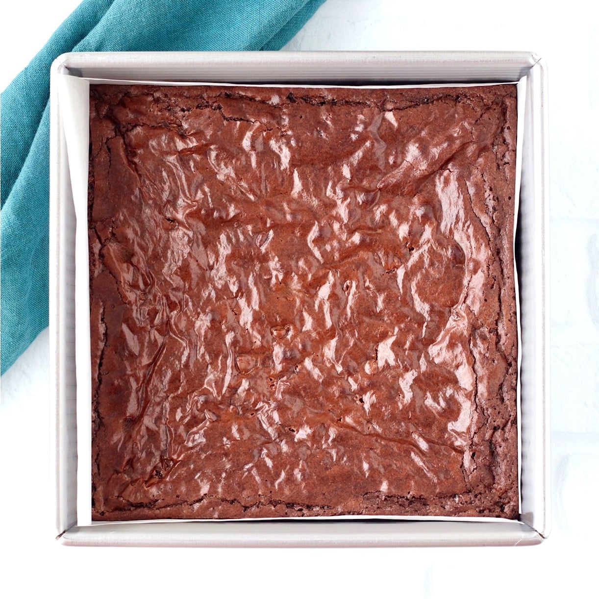 Baked chocolate chip brownies in square baking pan with napkin to the side.