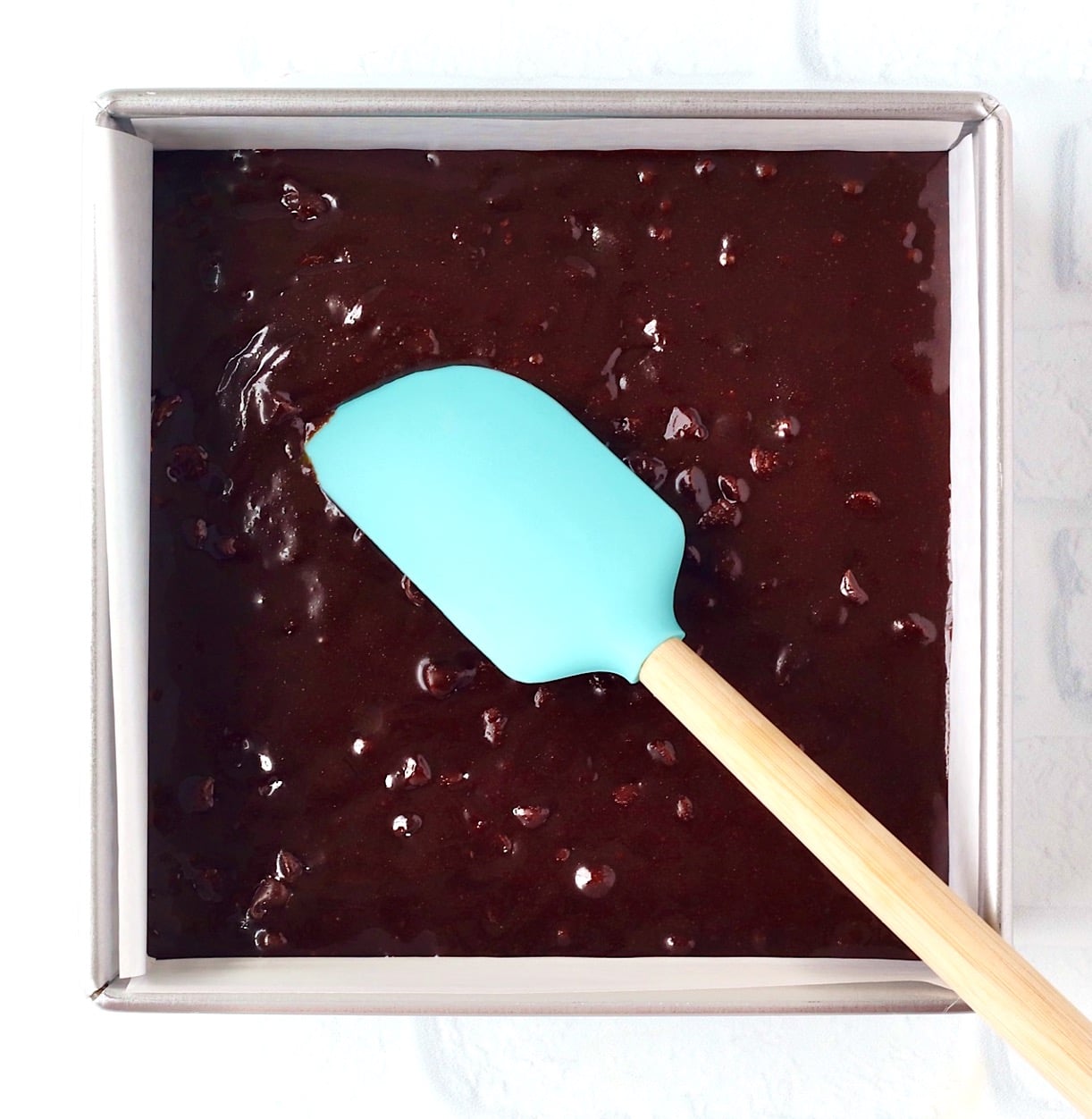 Chocolate chip chocolate brownie batter in pan with spatula.