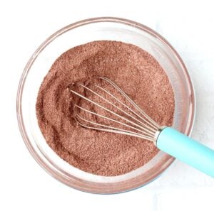 Cocoa powder brownie ingredients in mixing bowl with whisk.