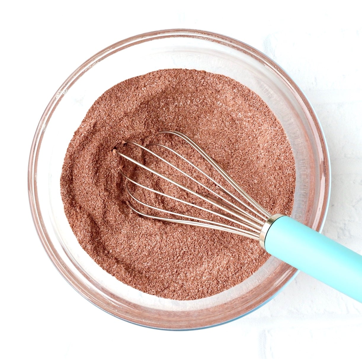 Cocoa powder brownie ingredients in mixing bowl with whisk.