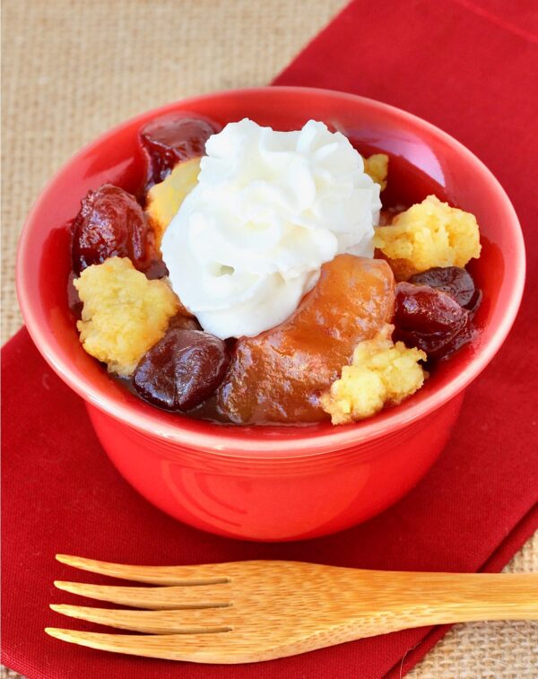 Apple Cranberry Dump Cake in small bowl with whip cream on top.