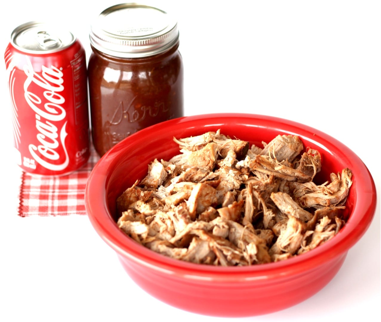 BBQ Shredded pork in bowl with barbecue sauce and soda in the background.