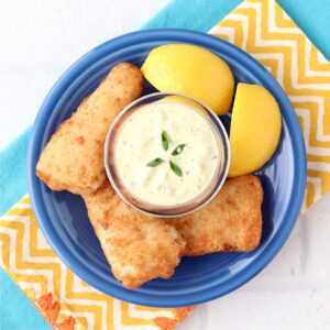 Homemade tartar sauce in small dish surrounded by crispy fish and lemon wedges.