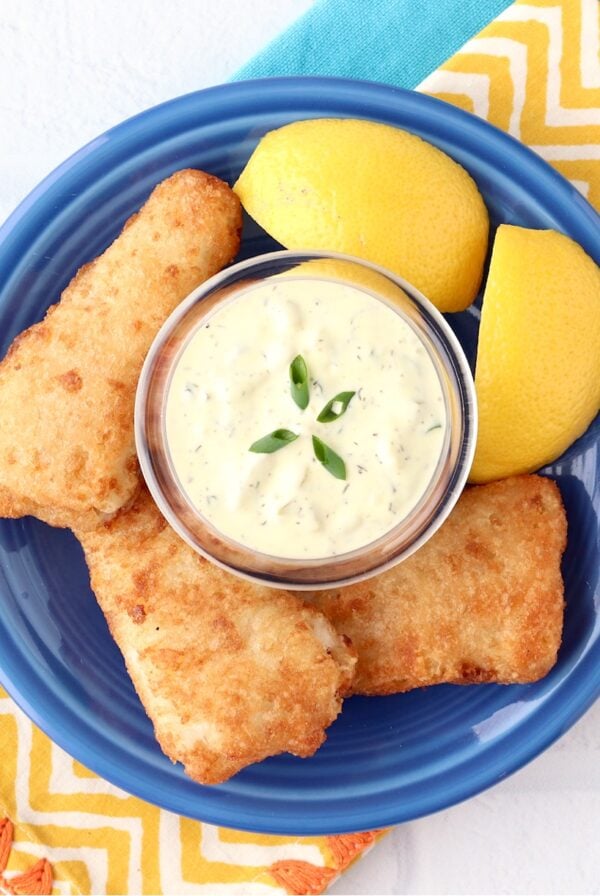 Homemade tartar sauce in small dish surrounded by crispy fish and lemon wedges.