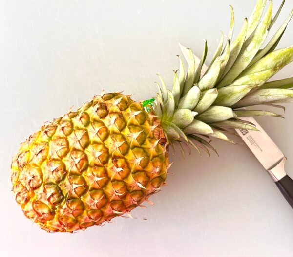 Pineapple on cutting board with knife.
