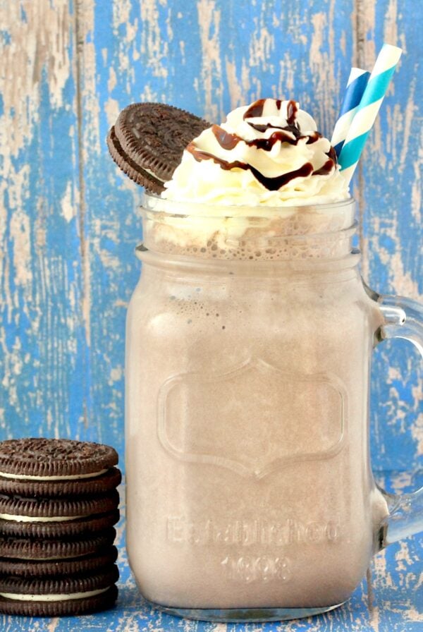 Oreo Milkshake in mason jar mug with whip cream, chocolate syrup, and Oreo cookie on top.