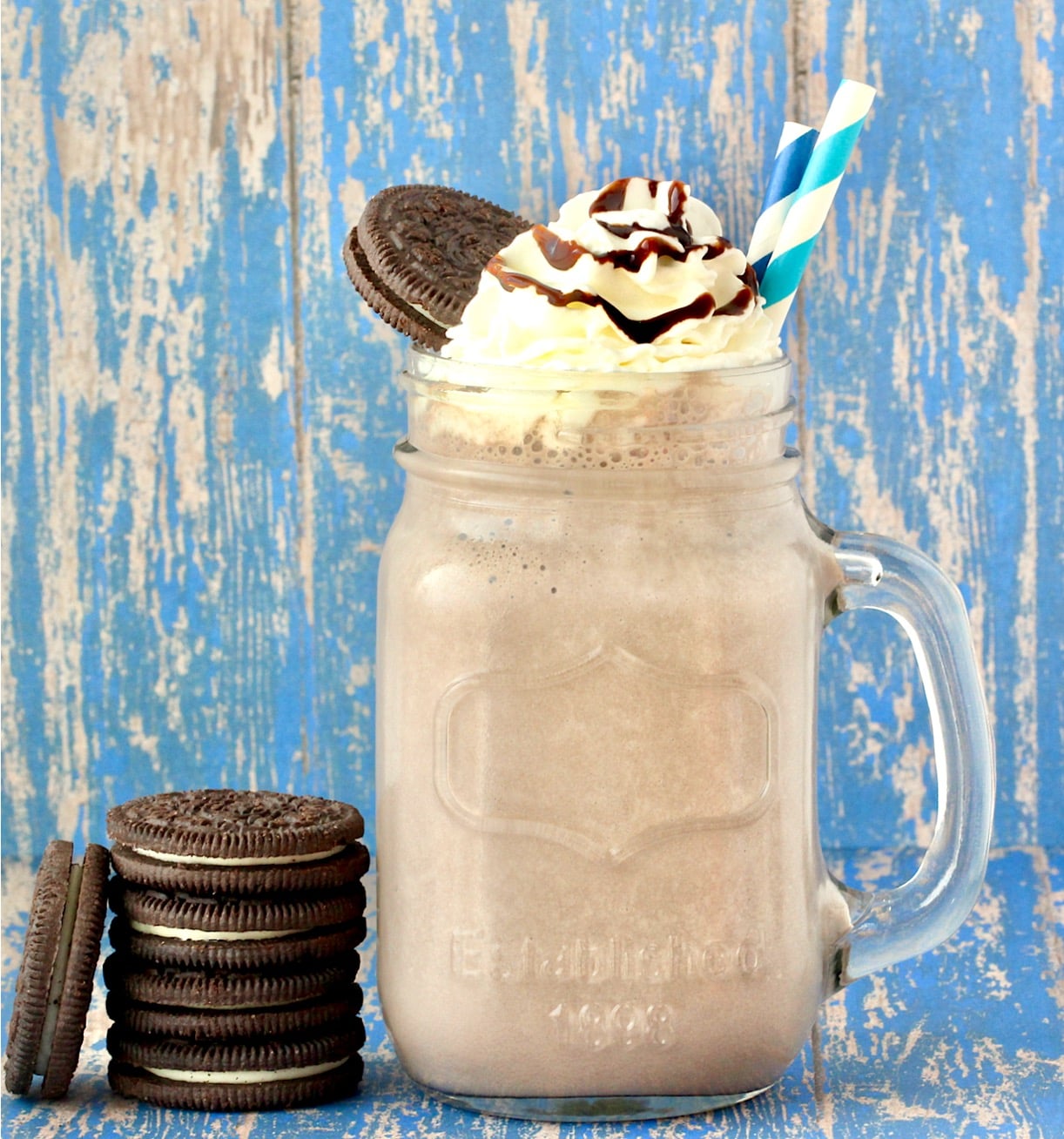 Oreo Milkshake in mason jar mug with whip cream, chocolate syrup, and Oreo cookie on top.